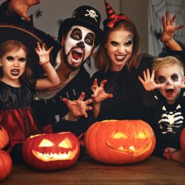 Family celebrating Halloween in traditional witch, skeleton costumes, with pumpkins in front of them