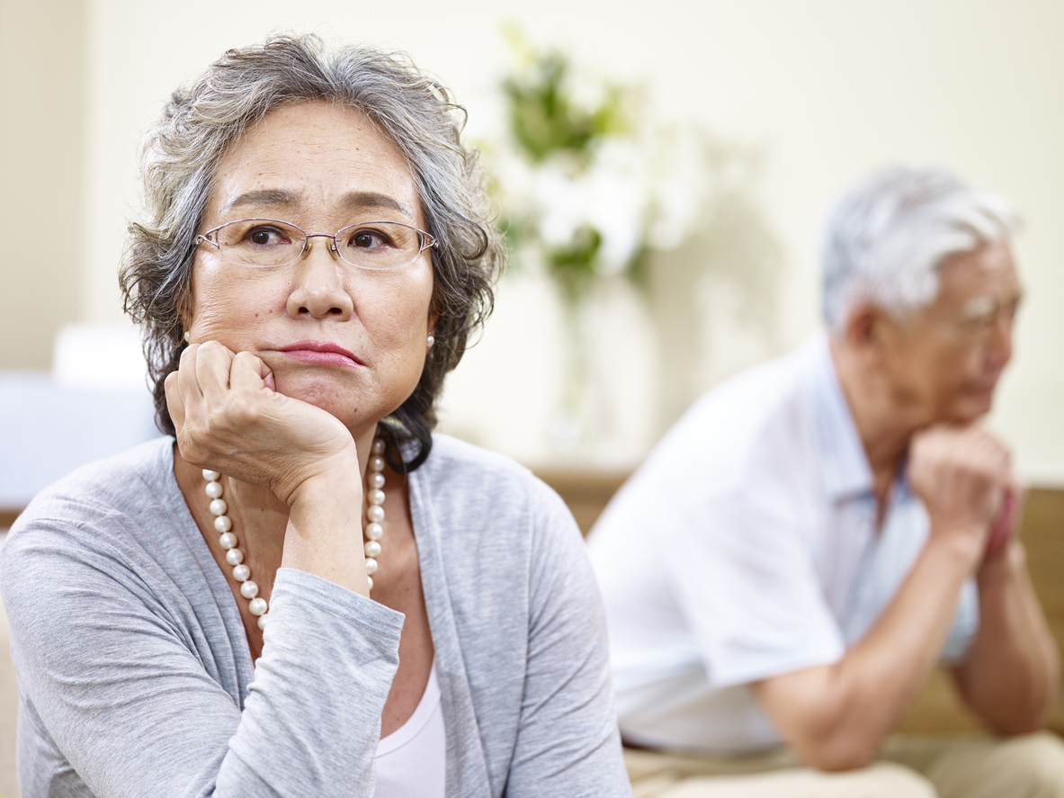 senior asian couple sitting on couch at home, angry at each other