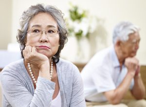 senior asian couple sitting on couch at home, angry at each other