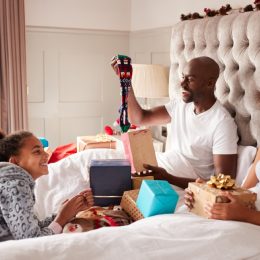 black woman, man, and two children opening presents in bed