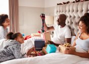 black woman, man, and two children opening presents in bed