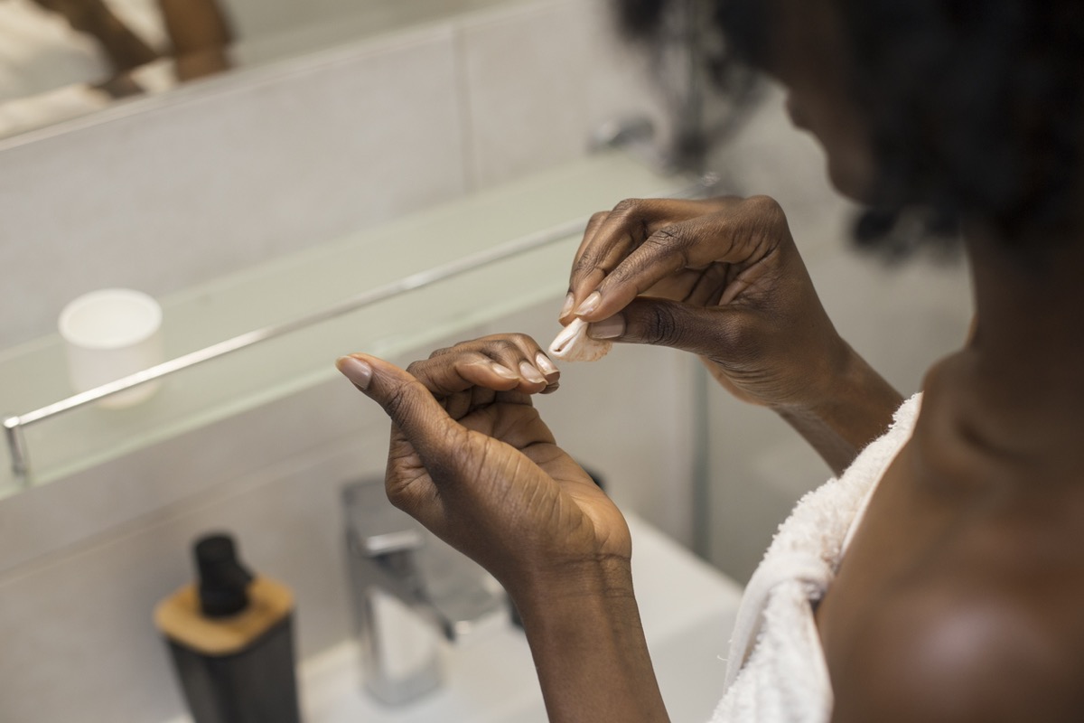 Black woman looks at fingernails while removing her nail polish.