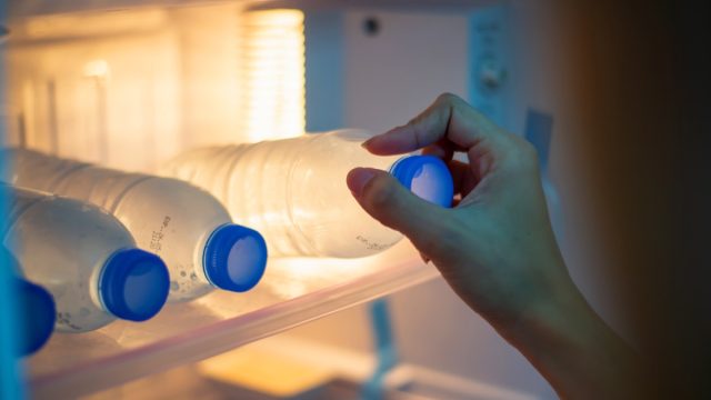 woman grabbing a bottled water in the fridge