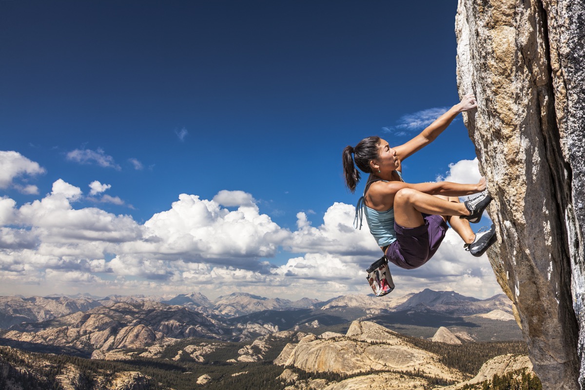Female climber dangles from the edge of a challenging cliff.