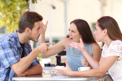 two women and a man sitting at a table arguing