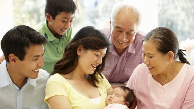 asian family looking at woman holding new baby