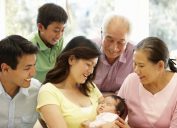 asian family looking at woman holding new baby