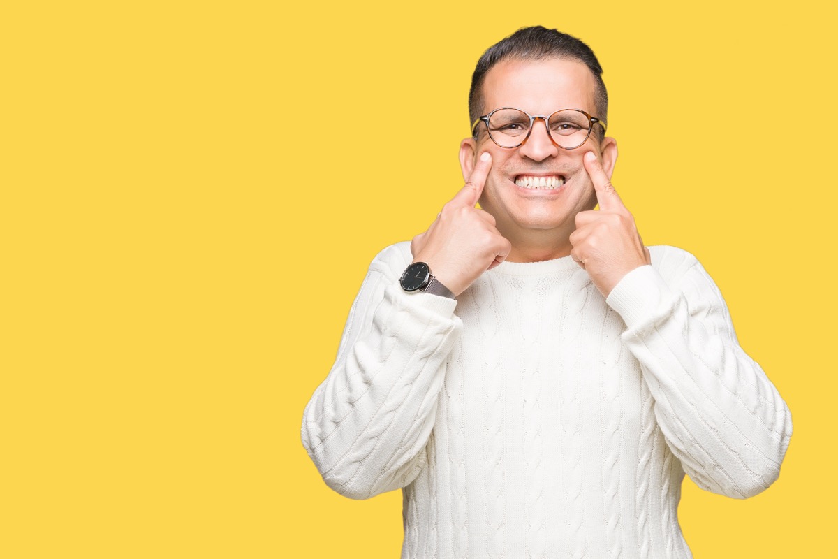 older man forcing a smile on yellow background