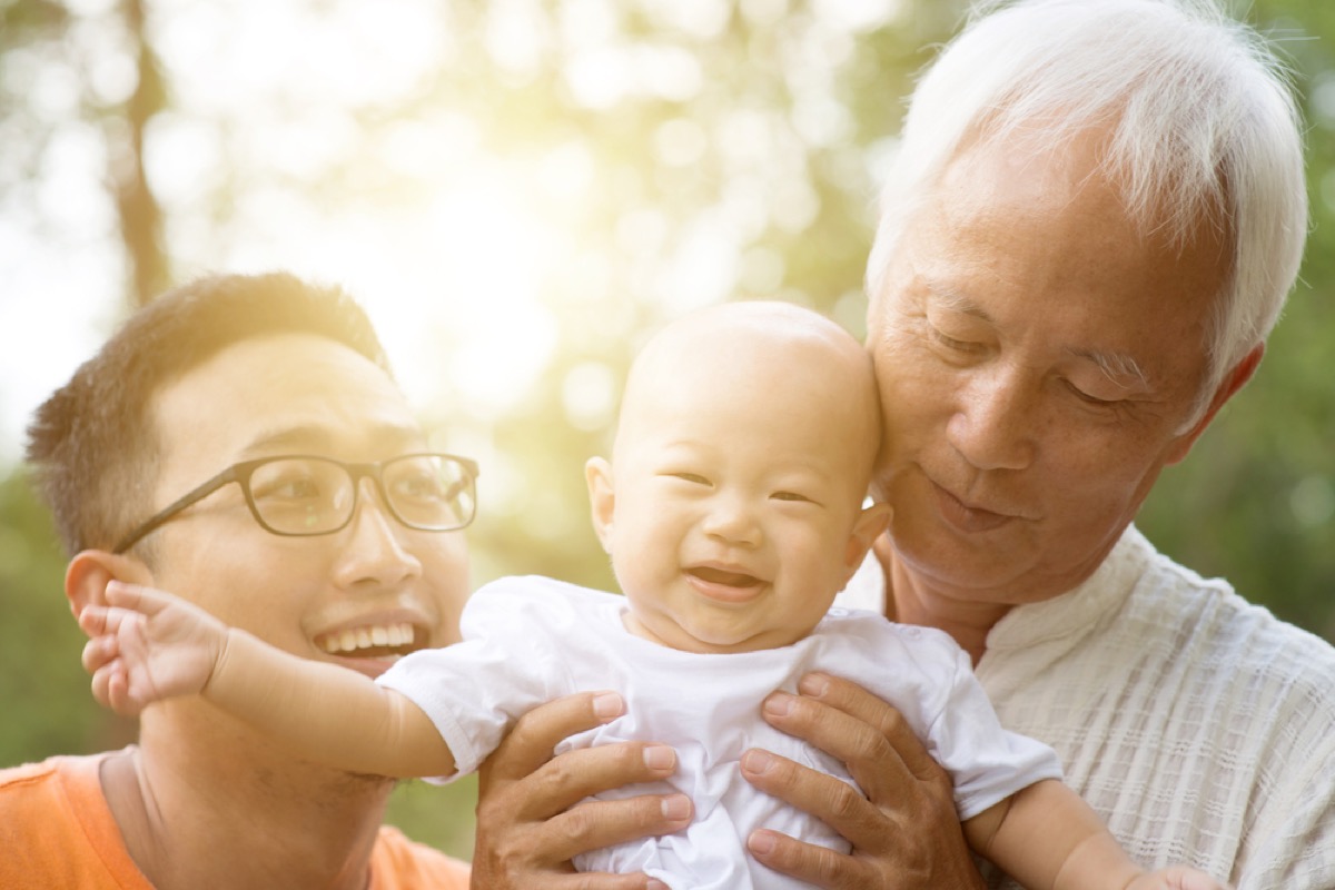 asian father and grandfather holding baby in white shirt