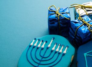 blue hanukkah cookie with menorah on it next to two small gifts wrapped in blue metallic paper and gold ribbon, hanukkah gifts