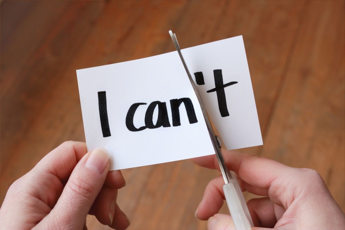 hands shown cutting paper with scissors that reads "i can't" so that it becomes "i can"