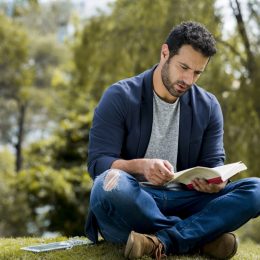 young latino man reading a book by himself in the park