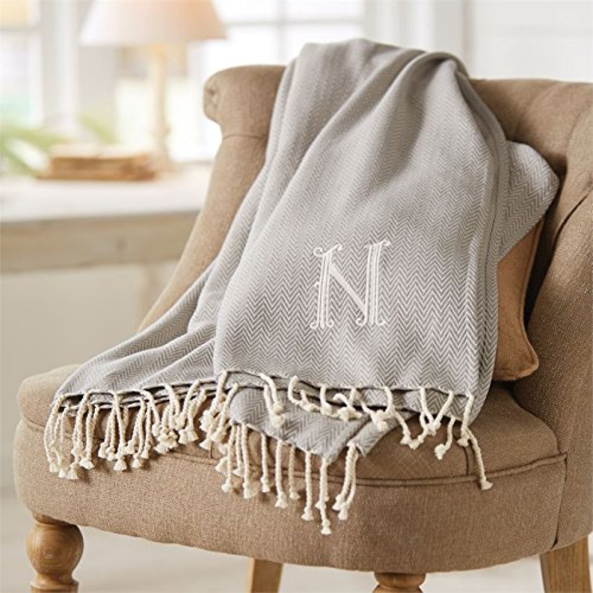 gray throw blanket with monogrammed N and white fringe on brown chair