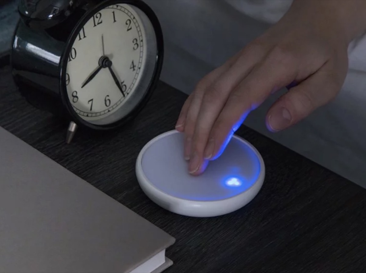 hand touching round device on tabletop with analog alarm clock, better sleep essentials