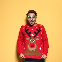 man in red reindeer sweater standing against yellow background