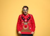 man in red reindeer sweater standing against yellow background
