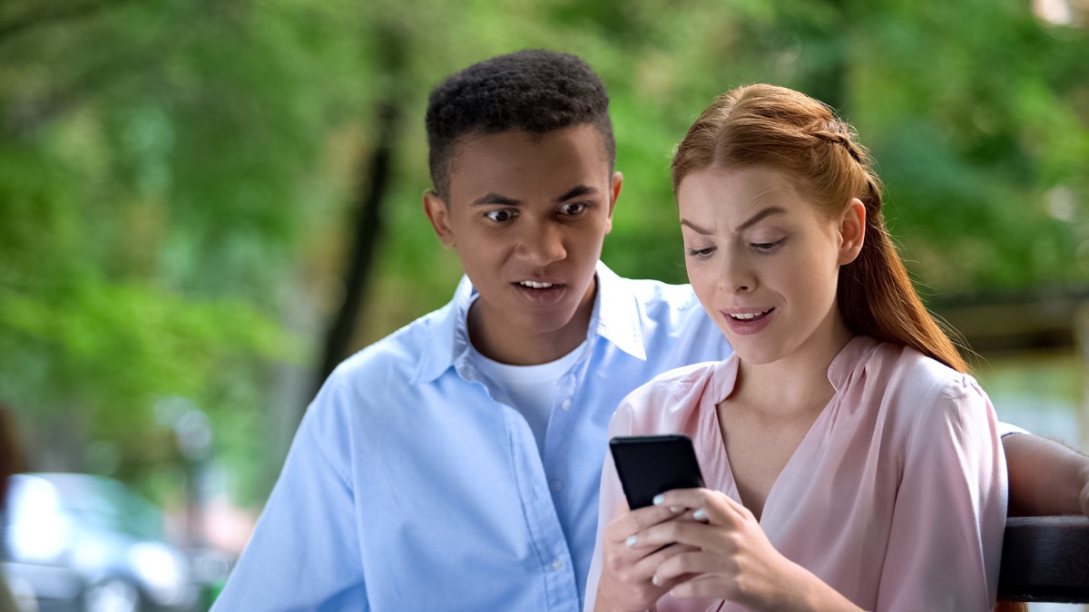 Shocked mixed-race teen couple watching social network photos through phone