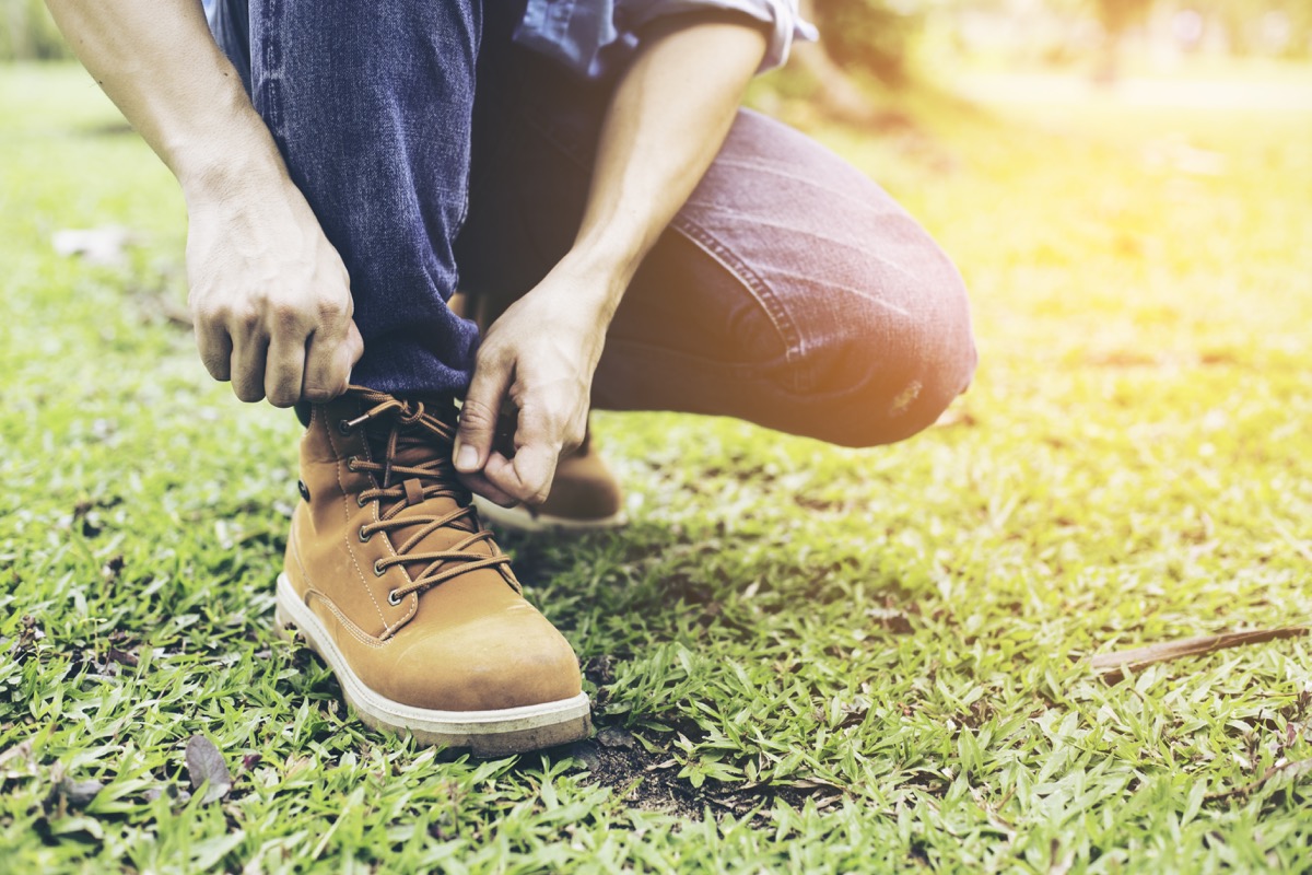 man in blue jeans tying brown work boot while kneeling down on grass lawn