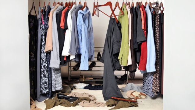 very unorganized and messy clothes closet. Shoes, sweaters, hangers and panty hose are lying on the floor. A pair of slacks and a dress shirt are about to fall off their hangers.