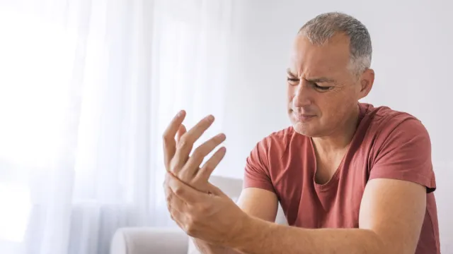 Mature man suffering from wrist pain at home while sitting on sofa during the day