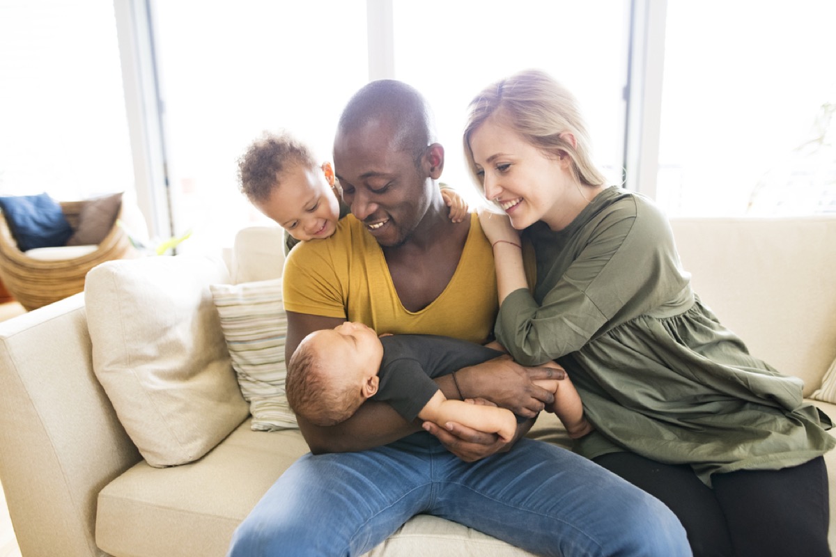 white mother and black father with mixed race toddler and infant sitting on couch