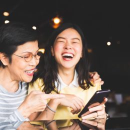 asian mother and daughter looking at a phone screen together, laughing in a cafe