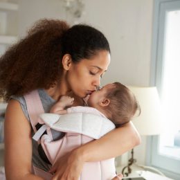 black mother kissing baby in pink carrier