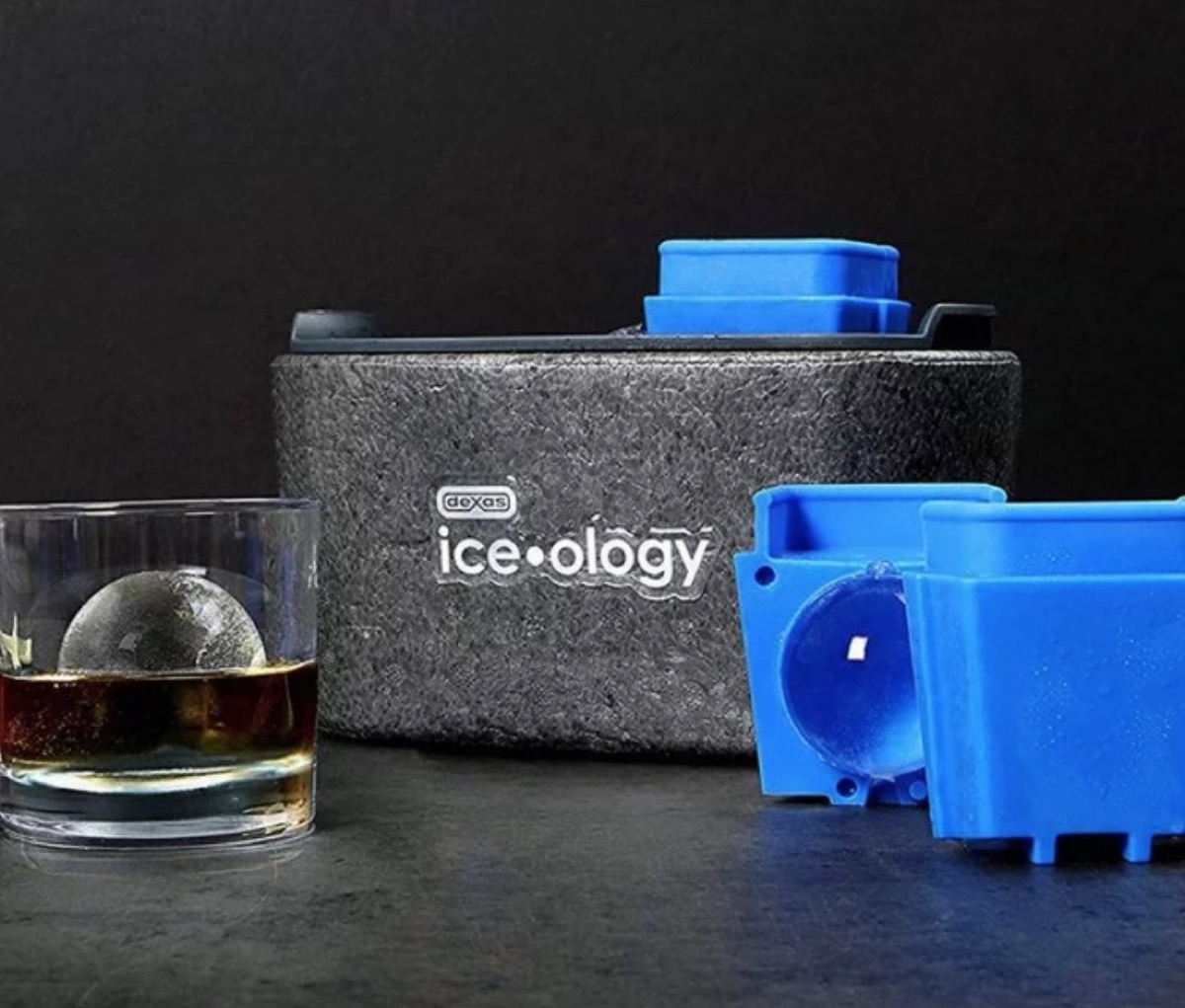 glass with whiskey and round ice cube next to blue ice cube mold