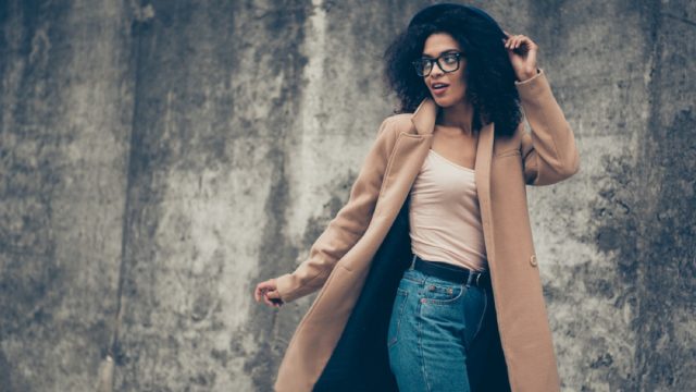 stylish black woman standing outdoors in camel coat