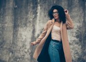 stylish black woman standing outdoors in camel coat