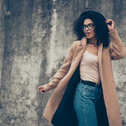 stylish black woman standing outdoors in camel coat