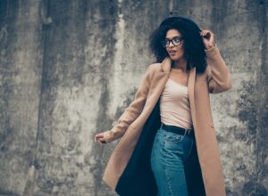 stylish black woman standing outdoors in camel coat