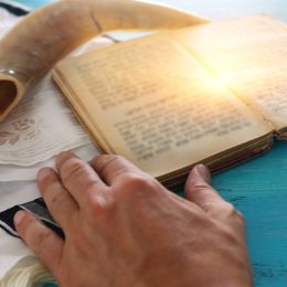 man reading torah with tallit and shofar behind it