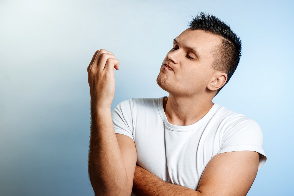 Portrait of a white man on a light background, looking at his nails. 