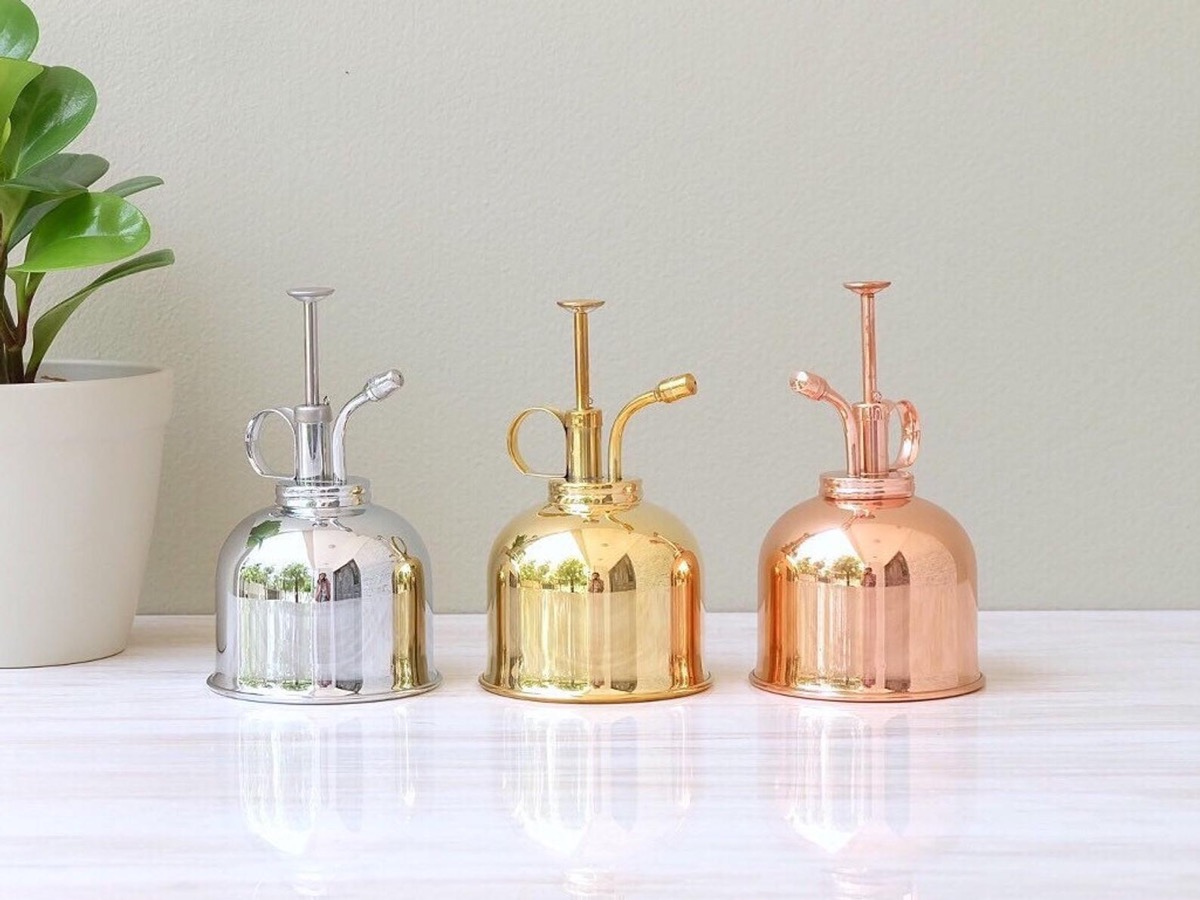 three vintage plant misters in silver, gold, and copper