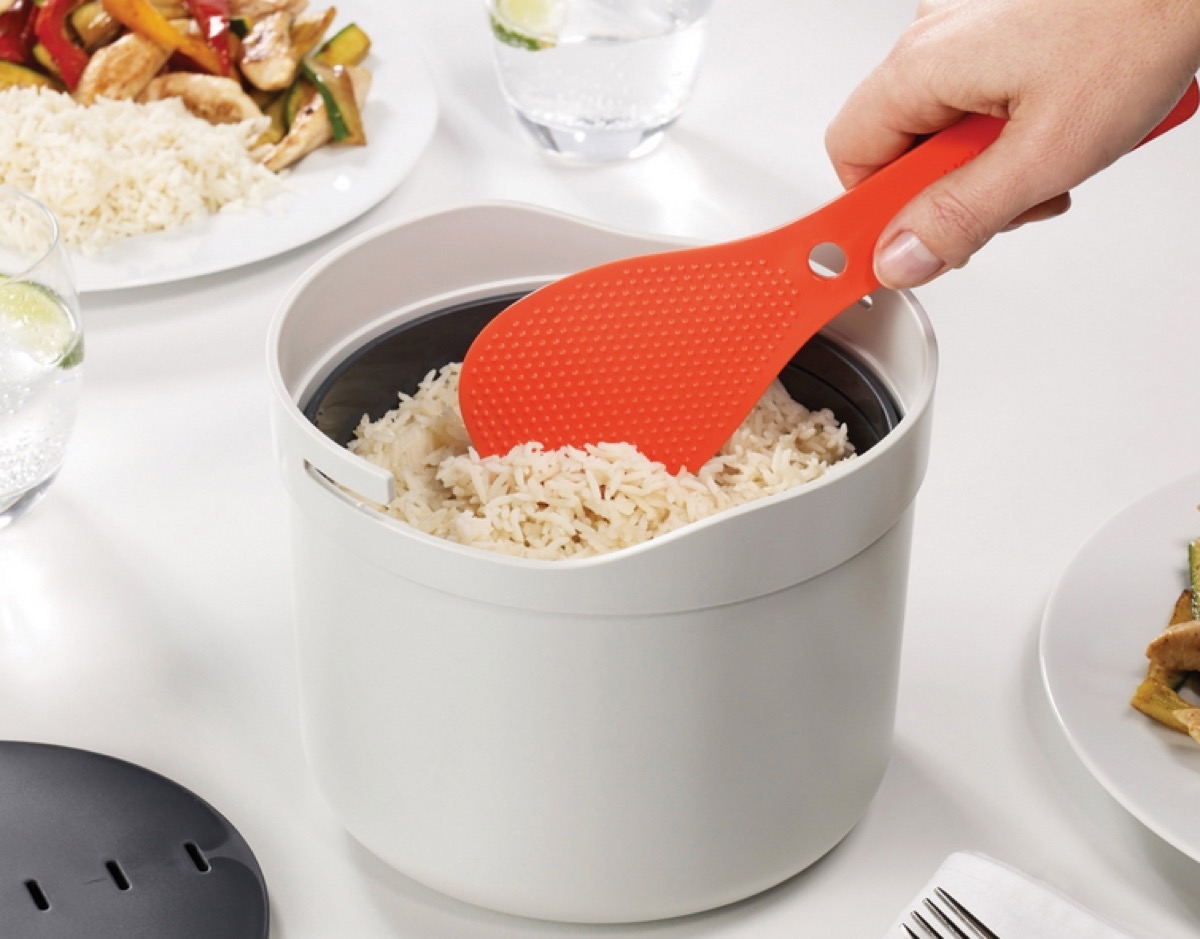 white hand using orange spoon to spoon rice out of white ceramic container