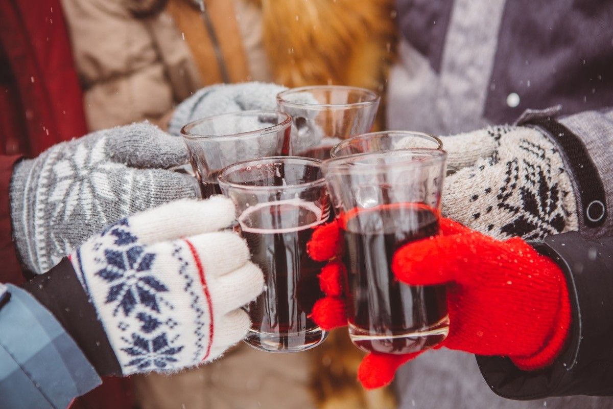 a group of friends in winter gloves tapping alcohol glasses in cheers