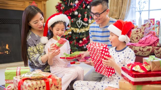 asian family with mother and father opening christmas presents with young boy and girl in santa hats