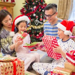asian family with mother and father opening christmas presents with young boy and girl in santa hats