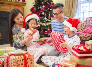asian family with mother and father opening christmas presents with young boy and girl in santa hats