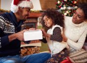 black man and woman in santa hats with little girl opening gifts