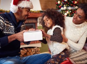 black man and woman in santa hats with little girl opening gifts