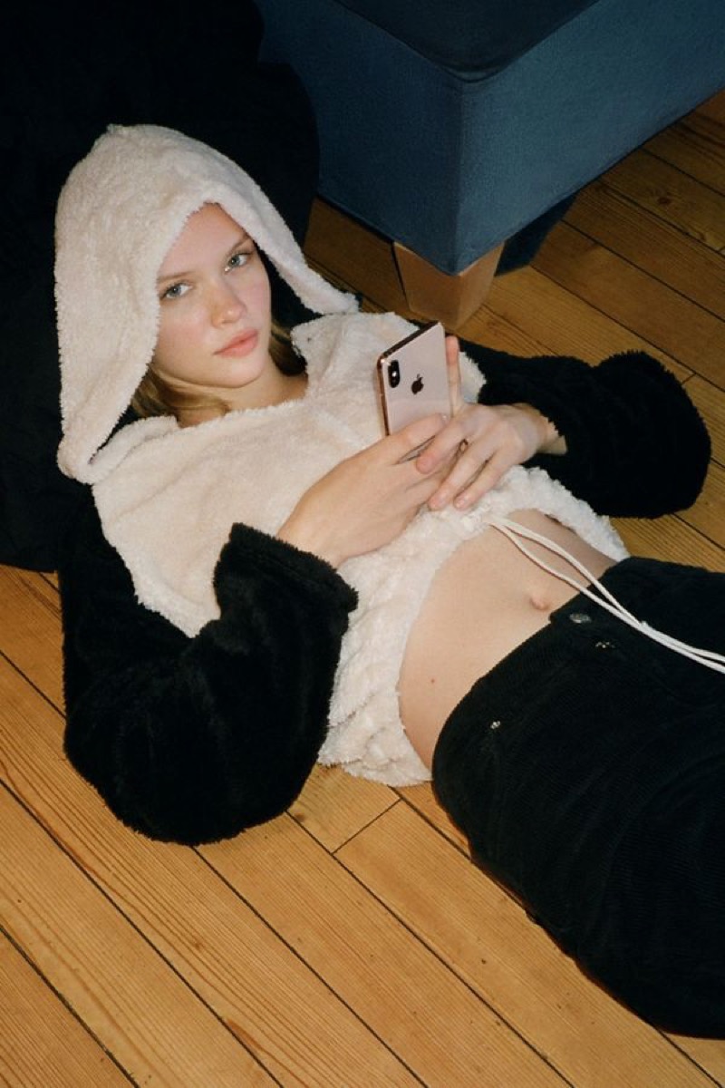 woman wearing black and white hoodie lying on floor holding iphone