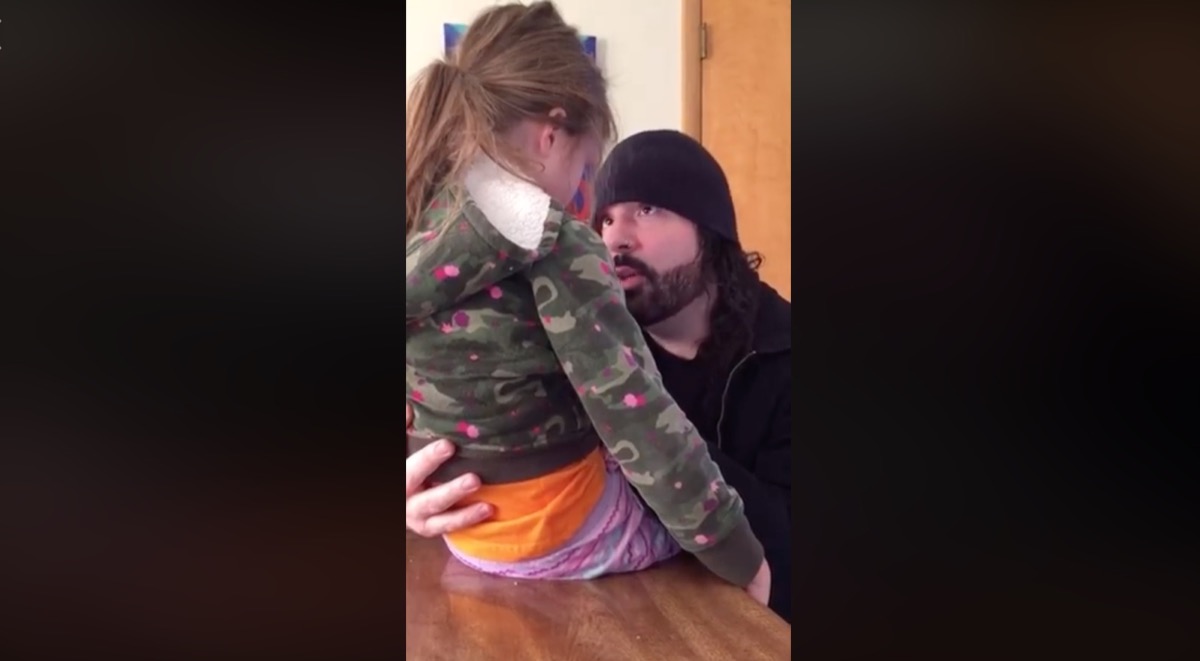 white man with beard and hat talking to young girl sitting on table
