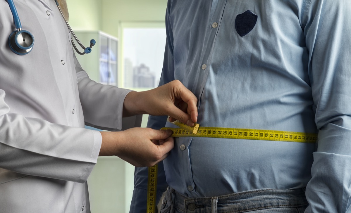 doctor measures waistline of overweight man