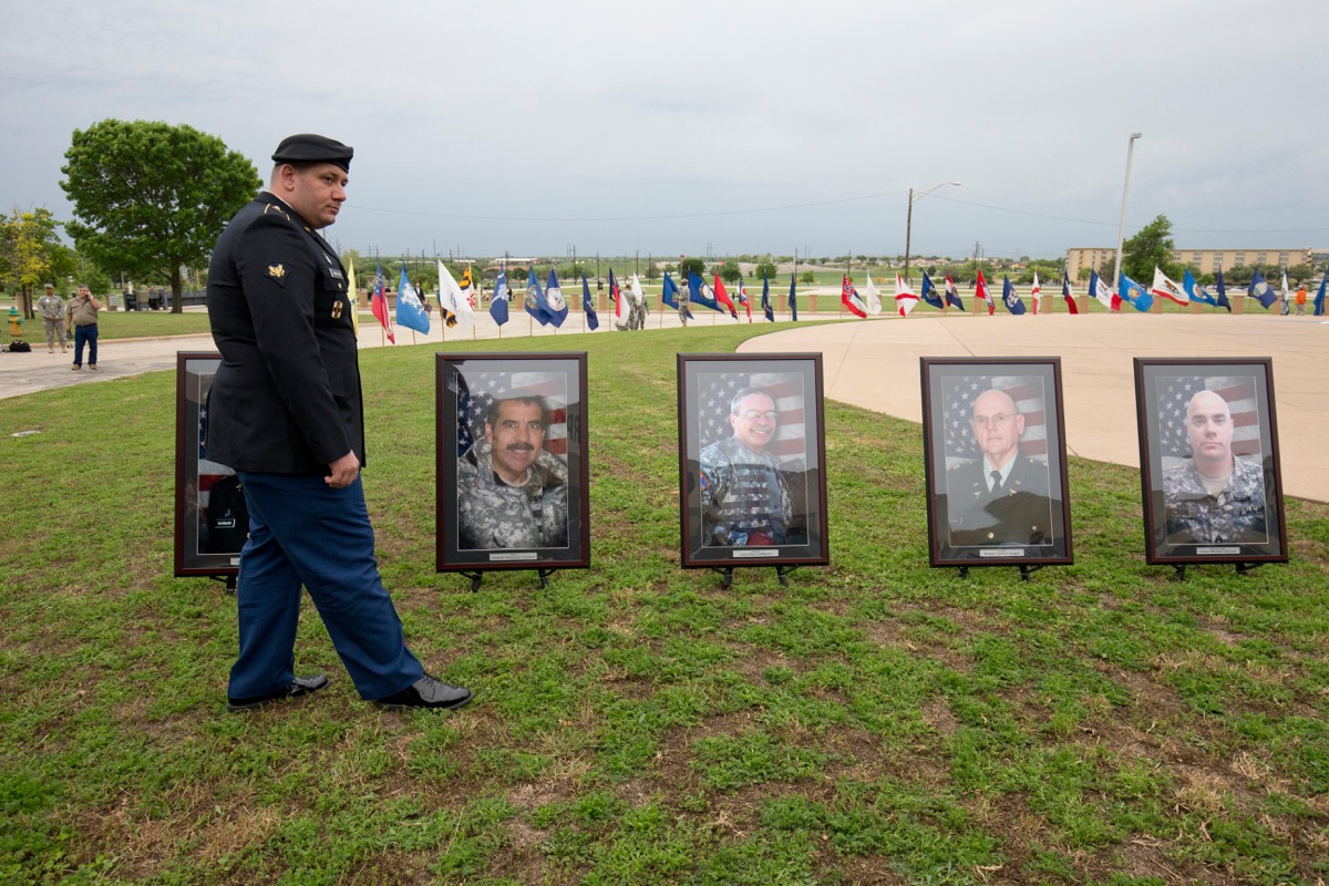 Soldier wounded in 2009 terrorist attack at Fort Hood TX stands before portraits of those killed in attack at memorial service