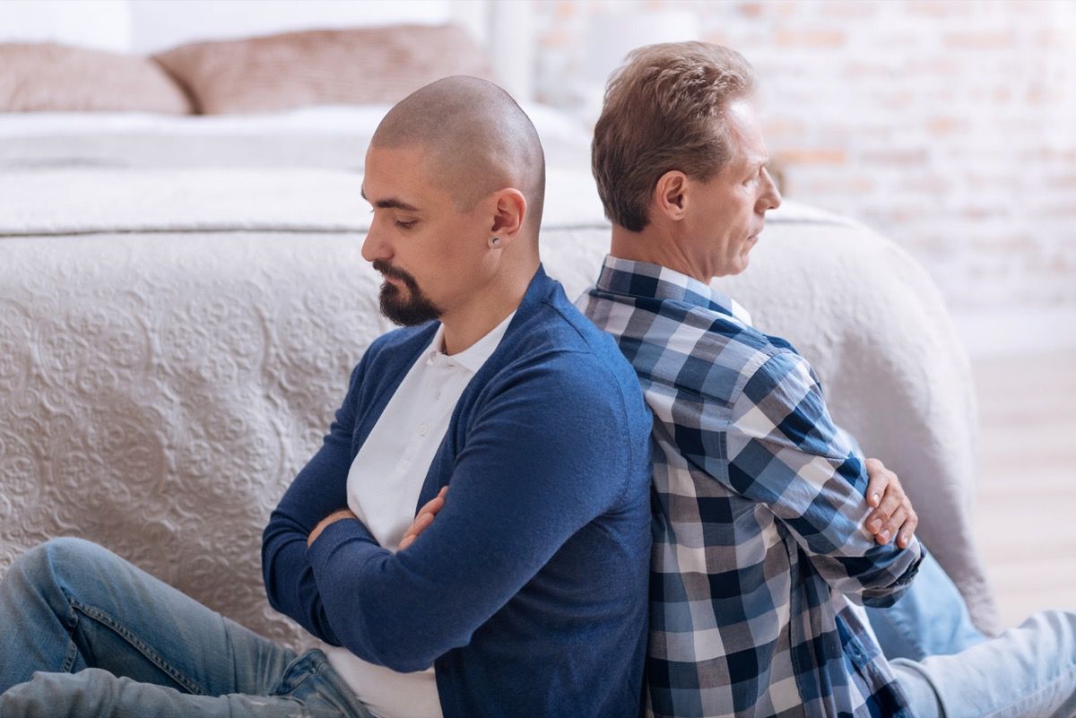 Upset disappointed thoughtful gay couple sitting on the floor back to back with crossed arms