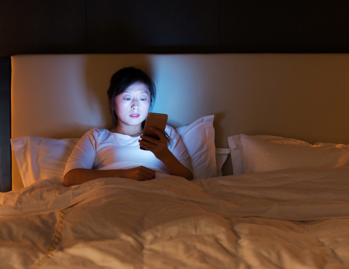 asian woman looking at her phone in bed