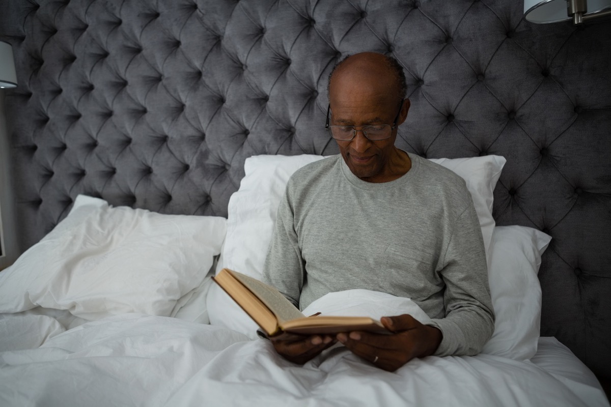 older man reading a book in bed