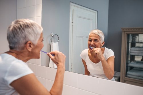 older white woman brushing her teeth in the mirror